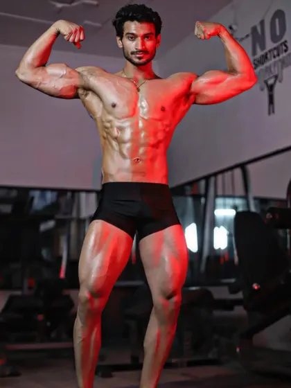 A front double biceps pose under dramatic lighting. This is the result of a consistent muscle gain transformation plan and relentless effort.