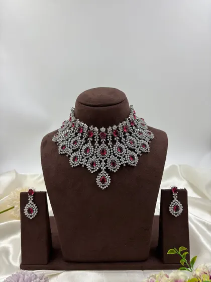 A heavy, silver-plated AD necklace set with a peacock-inspired feather design. This statement piece is available in blue, green, pink, and all-white.