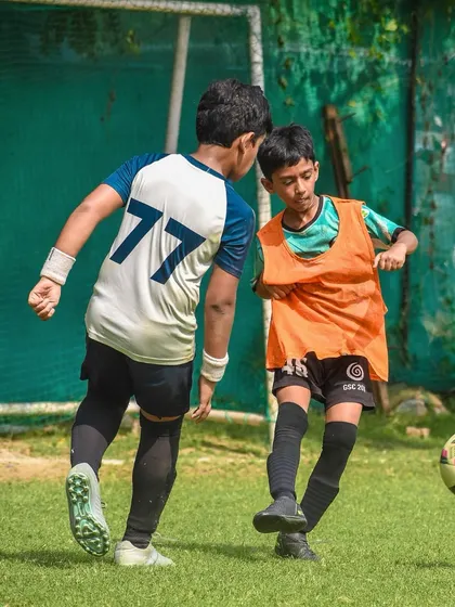 A player in an orange bib shields the ball from a defender.