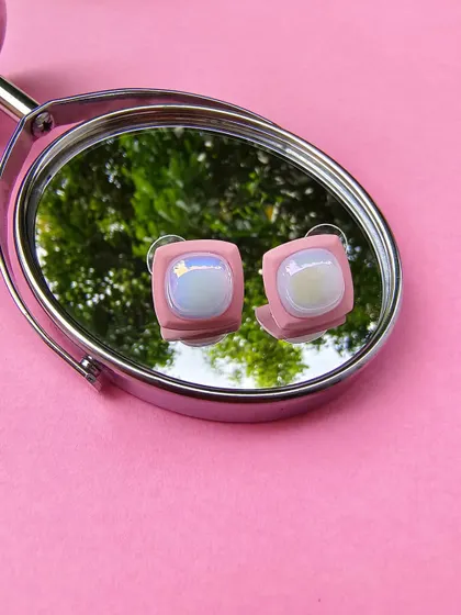 A product shot of the pink enamel square earrings, as seen on Karishma Tanna, reflected in a mirror.