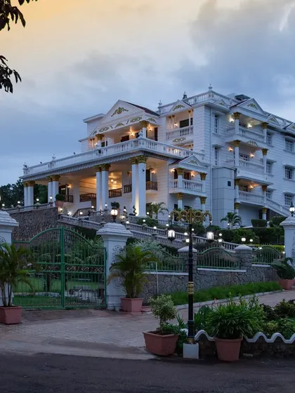 A full view of the palatial residence at dusk. The lighting design highlights the multiple levels, balconies, and the grand staircase leading up to the main entrance.