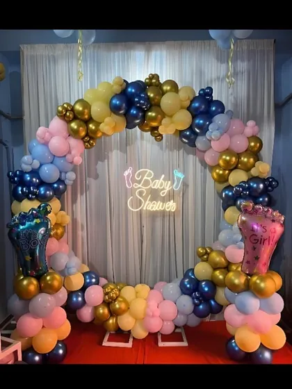 A baby shower balloon ring in navy blue, light blue, pink, and gold. The setup includes foil balloons shaped like baby feet.