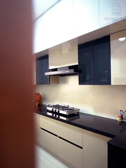 A minimalist parallel kitchen featuring handleless beige cabinets and a sleek black countertop. The design is clean and uncluttered, with a built-in chimney and under-cabinet lighting ensuring a functional and aesthetically pleasing cooking environment.