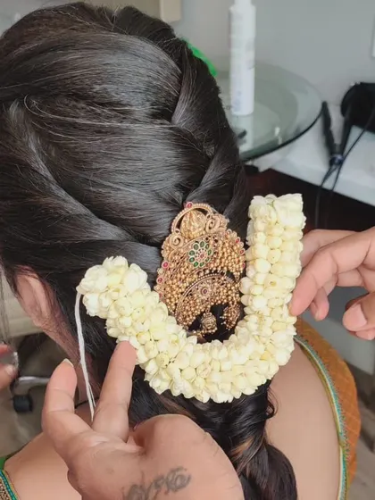A close-up shot of my hands carefully placing a jasmine gajra around a traditional gold hairpiece.