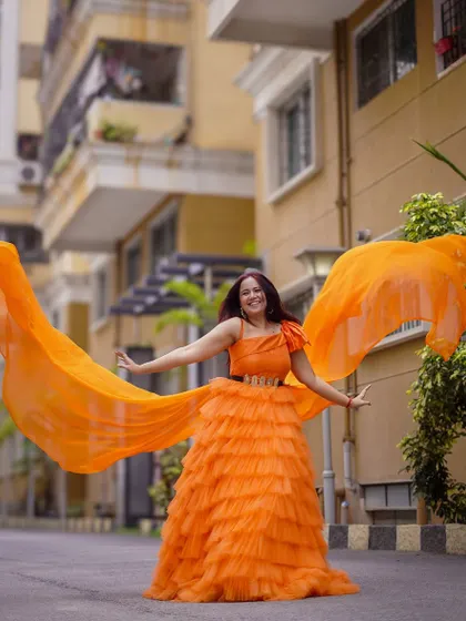 This vibrant orange tiered ruffle gown is a bold and beautiful choice for any celebration. The attached wings add a touch of drama and fun.