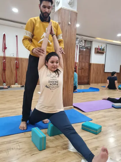 I am helping a student find the right alignment in her supported split. Hands-on adjustments are key to ensuring students practice safely and effectively.