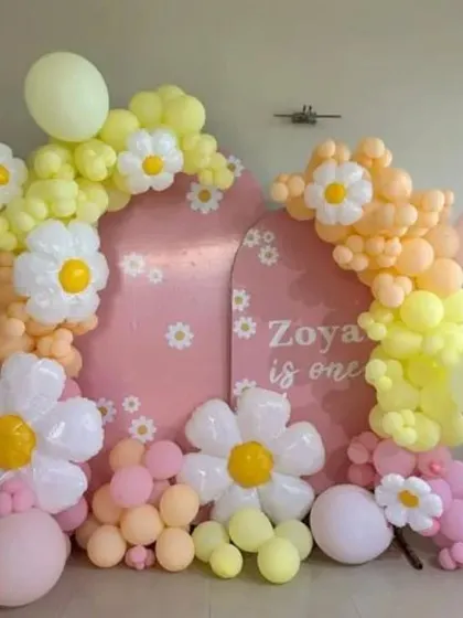 A daisy-themed first birthday party with a pink arched backdrop and balloon flowers in pastel colors.