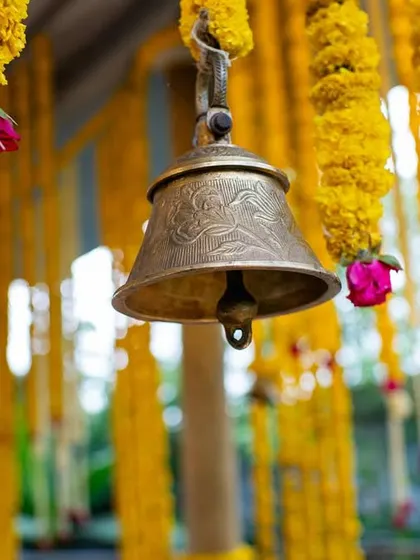 It's the small details that complete the theme. A close-up of a traditional brass bell hanging amidst garlands of marigold flowers, adding an authentic touch to the Haldi decor.