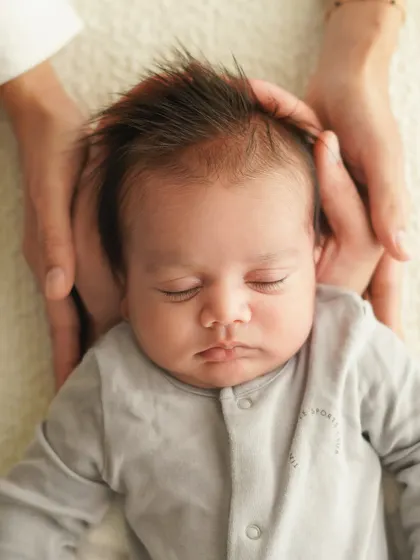 Another angle of parents' hands cradling their baby's head, focusing on the newborn's peaceful, sleeping face.