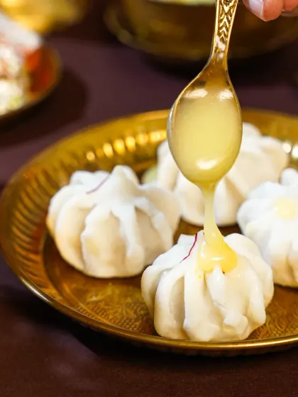 A decadent stream of golden ghee being poured over delicate, steamed Modaks. This action shot is both luxurious and traditional, capturing a key moment in enjoying this festive sweet.
