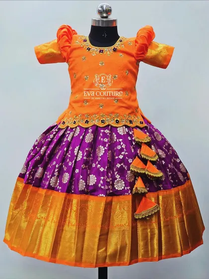 A festive orange and purple lehenga. The orange peplum blouse has delicate maggam work, and the purple Banarasi skirt is finished with a wide orange and gold border.