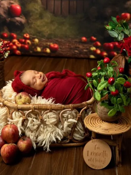Celebrating one month with a sweet apple-themed photoshoot. This little one is all smiles, nestled in a basket surrounded by fresh apples and red flowers.