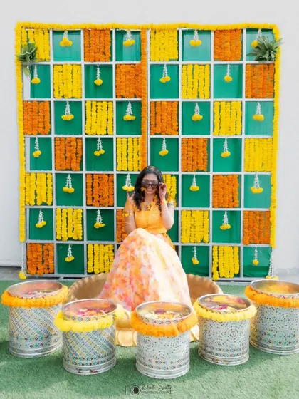 A wide shot of the bride at her Haldi ceremony, showing the full scale of the beautiful marigold decor. This photo captures the vibrant and festive atmosphere of the event.