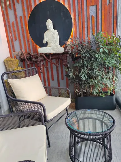 Another angle of the Zen-inspired balcony, showing the comfortable seating arrangement next to the Buddha statue and a large planter with a China Doll plant, perfectly blending comfort and spirituality.