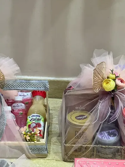 Two hampers from a trousseau collection, one with juices and another with dry snacks. The coordinated wrapping with pink net and floral details ensures even everyday items look special.
