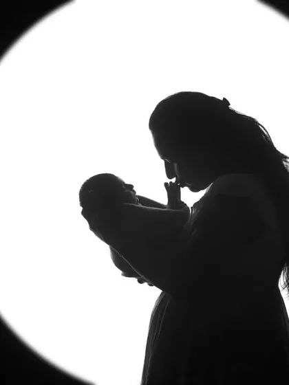A mother's silhouette, holding and gazing at her newborn baby. The backlighting creates a halo effect, emphasizing the sacredness of this first connection.
