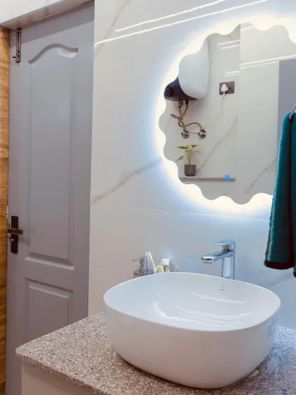 This image highlights the details of a modern bathroom, including a backlit mirror with a built-in shelf and a convenient power socket for a hairdryer.