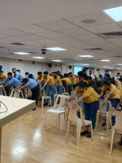Employees at Volvo use chairs for support in a forward-bending exercise. This demonstrates how we adapt classical yoga poses for the office environment to ensure safety and accessibility.