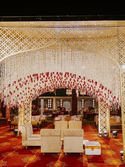 An enchanting entrance for a royal wedding, featuring a canopy of cascading white and red flowers. This design, set against the backdrop of The Leela Palace, creates a magical and opulent welcome for guests.