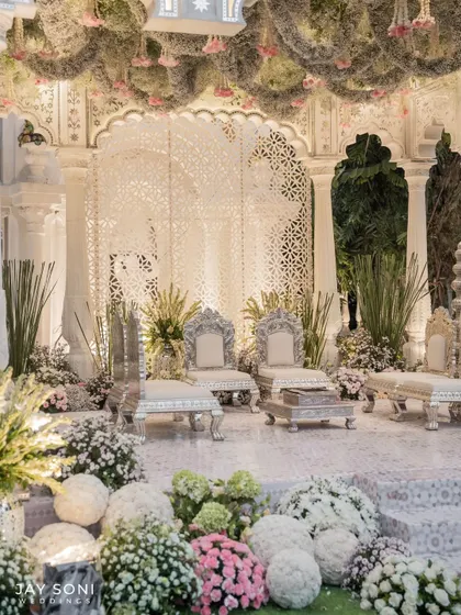 For this wedding, I designed a mandap that exudes ethereal elegance. It features intricate white jaali screens, ornate silver chairs for the couple, and a ceiling adorned with a thick layer of moss and hanging florals.