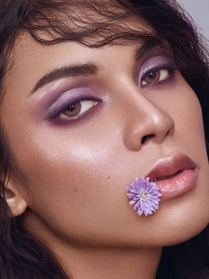 An artistic beauty concept where a wash of purple eyeshadow is paired with a delicate flower, creating a poetic and memorable image.