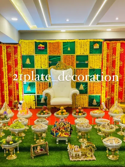 A full view of a traditional baby shower setup with a yellow and green checkered backdrop. The decor includes a white throne, dolls, and a complete arrangement of plates on an artificial grass carpet.