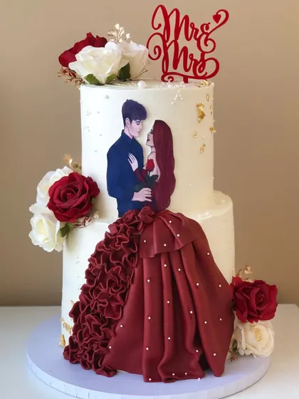 A two-tiered cake celebrating a couple, with a custom illustration and a dramatic red ruffled dress detail.