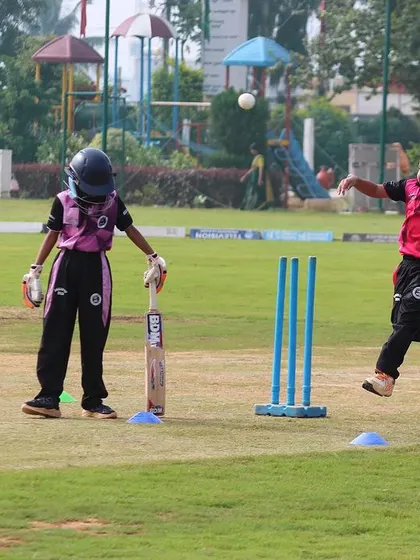 A young bowler in action during a U-10 drill, with a coach observing to provide guidance on technique.