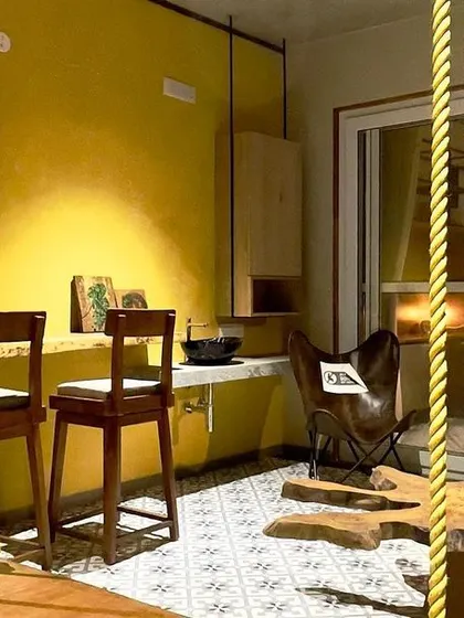 A vibrant terrace lounge designed for a residential space. The use of bright yellow walls, rustic wooden furniture, and a traditional swing creates a playful and eclectic relaxation zone.