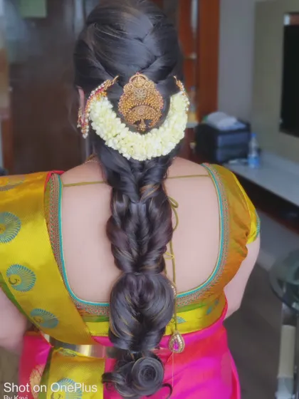 A voluminous, textured braid adorned with a traditional gold hairpiece and a semi-circular jasmine gajra.