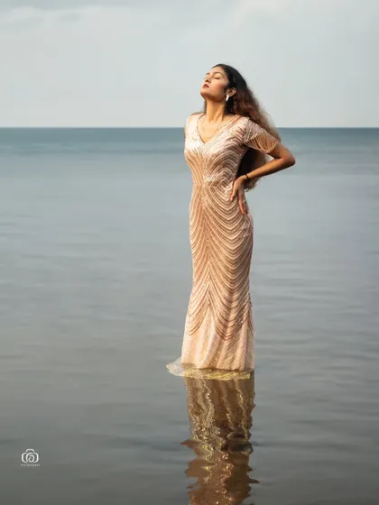 A powerful and serene image of a model standing in the ocean in a full-length gown. The reflection in the water and the vastness of the sea create a truly epic and cinematic shot.