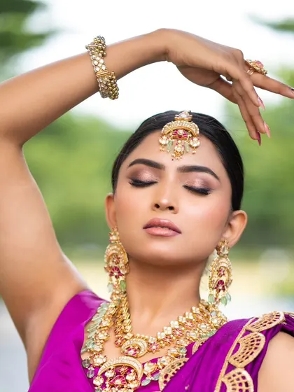 We help you choose the perfect jewelry to complete your outfit. This close-up shows how a stunning multi-layered necklace with pink and green stones beautifully complements the royal purple lehenga.