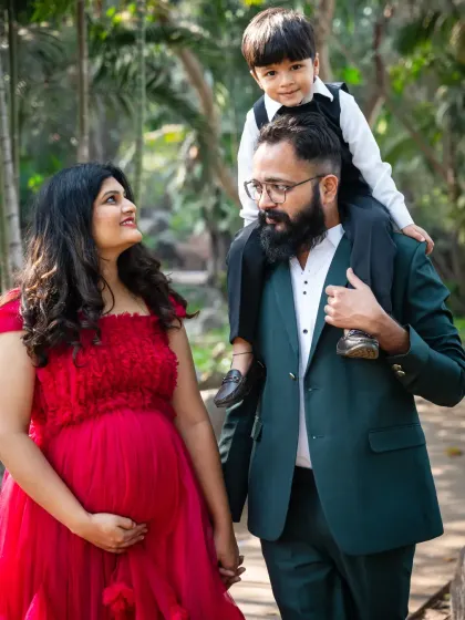 The family is growing. This heartwarming photo shows the mom-to-be in a beautiful red gown, hand-in-hand with her partner, who has their son perched happily on his shoulders.