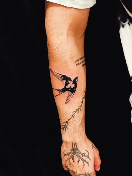 A detailed swallow tattoo on the forearm, with additional branch and root designs on the hand, creating a larger nature-themed composition.