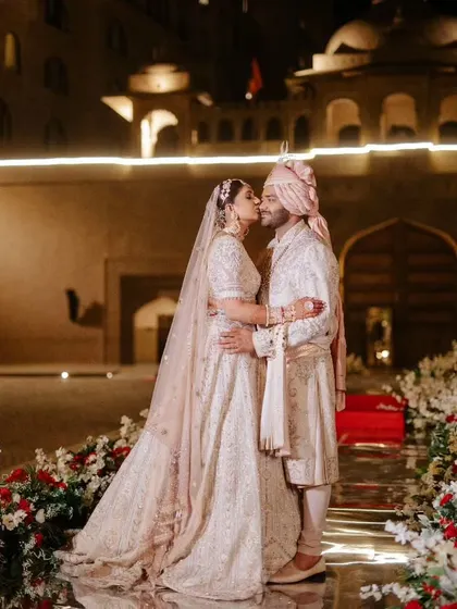A romantic kiss between the newly married couple, surrounded by a path of flowers against the illuminated palace.