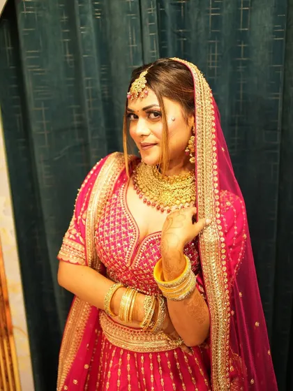 A close-up portrait of a bride in a rani pink lehenga. This highlights the matching gold jewellery and the happy glow of a bride who has found her perfect outfit.