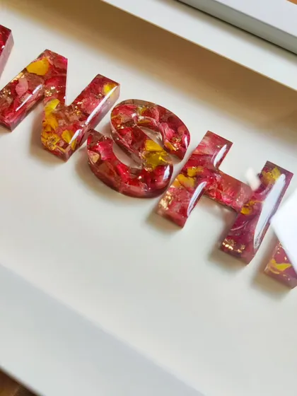 A close-up of the letters in the name shadow frame, showing the vibrant colors of the preserved flowers and the subtle sparkle of gold leaf.