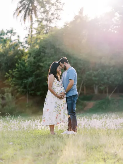 A full-length portrait of the couple standing in a field during golden hour. The soft, warm light and natural surroundings create a romantic and dreamy atmosphere.