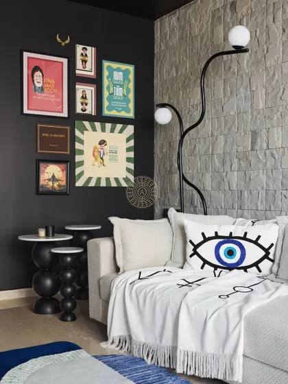 We created a cozy entertainment corner with black walls and a natural stone feature. The quirky gallery wall and evil-eye cushion add a playful and personal touch to this relaxing space.