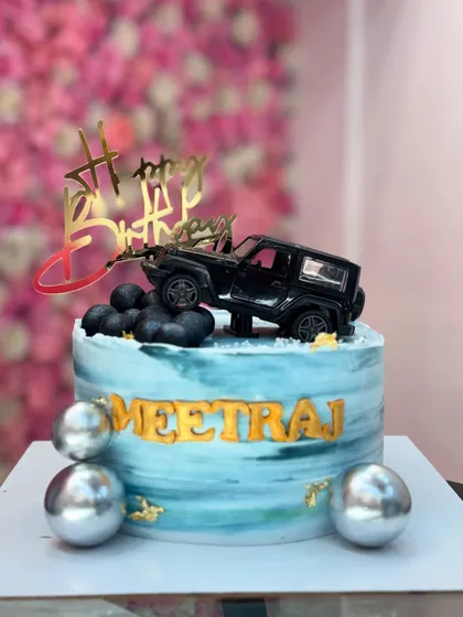 A fun cake for a Jeep lover, featuring a toy Thar on top of a blue marbled cake with silver spheres.