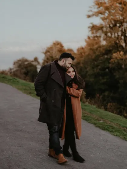 A couple shares a quiet, affectionate moment on a winding road in the hills, dressed in warm coats. This candid shot captures the feeling of a romantic walk during an autumn pre-wedding session.