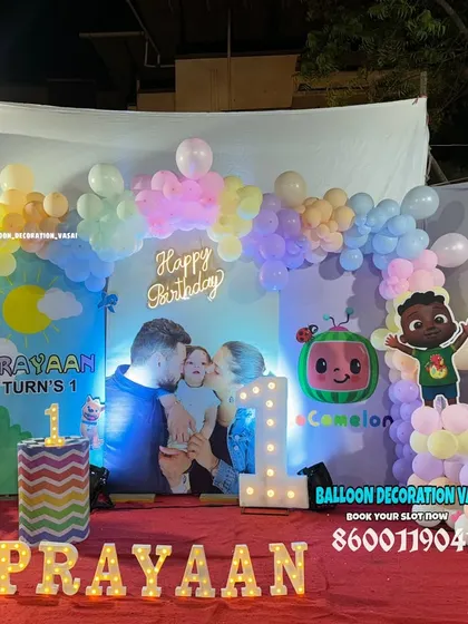 A Cocomelon theme for Prayaan's first birthday. This setup includes a custom photo backdrop, a pastel balloon arch, a neon sign, and light-up letters spelling the name.