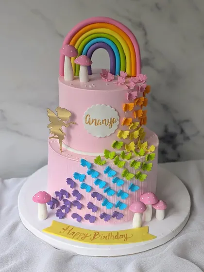 A whimsical two-tier cake with a cascade of rainbow-colored butterflies. This design also features a golden fairy silhouette and cute little mushrooms.
