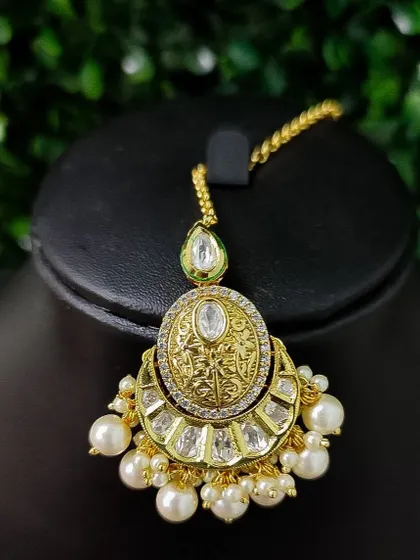 A crescent-shaped maang tikka with an engraved texture and large pearl drops. The simple design is both elegant and timeless.