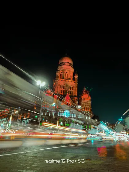 A long exposure shot of Mumbai's BMC building at night, with the light trails of buses creating a sense of speed and constant motion.