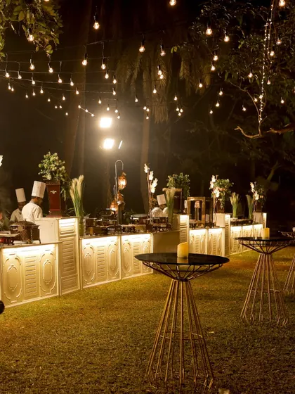 I transform venues into magical spaces. This is an evening reception setup with elegant food counters, ambient lighting, and high top tables, creating a sophisticated and inviting atmosphere for guests to mingle and dine.