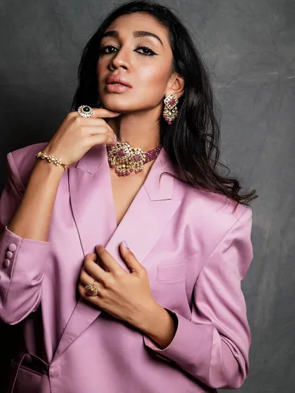 A close-up on the jewelry and the texture of the pink suit. Detail shots like this are essential for fashion and brand collaborations.