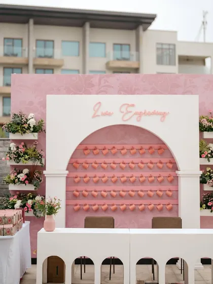 A live engraving station designed to be a feature of the decor, set against a pink backdrop with heart-shaped tags for a Bridgerton-themed tea party.