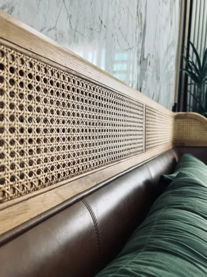 The rich texture of the genuine saddle nut leather on the Tierra Bed's headboard, contrasted with the natural rattan. These premium materials are chosen for their beauty and durability, creating a piece that is both luxurious and lasting.