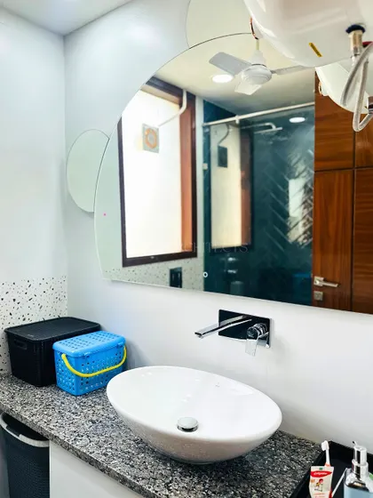 A functional and stylish bathroom with a unique, organically shaped mirror, a simple vessel sink on a granite countertop, and practical storage solutions.